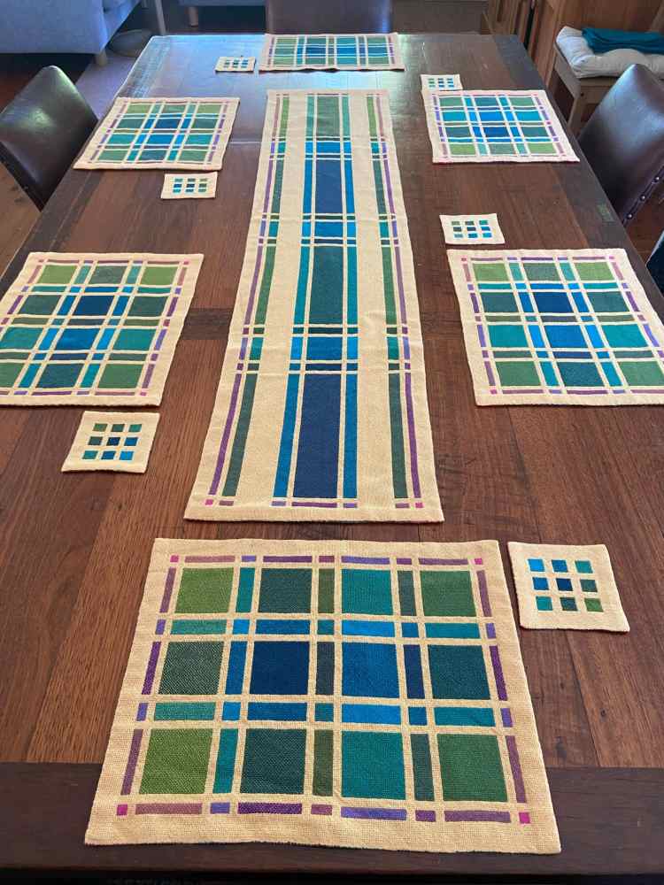 Photo of a long table with six place settings. There is a table runner with matching placemats in a green-blue colour scheme.