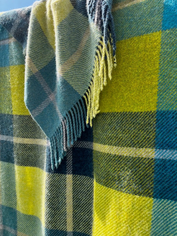A photo of a twill check blanket draped over a line. The colours are bright green, muted teal, navy and grey.