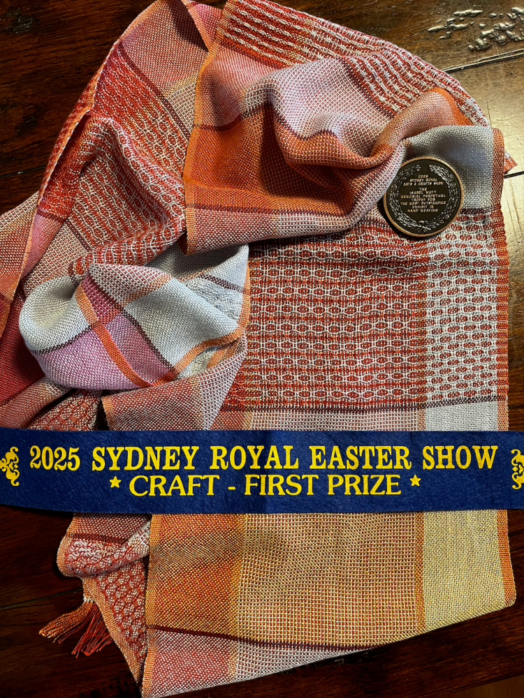 A photo of my winning scarf (oranges, silver and pinks) with the first place ribbon and a medal.